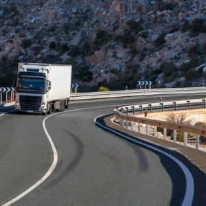 Camión blanco en una curva con una montaña detrás